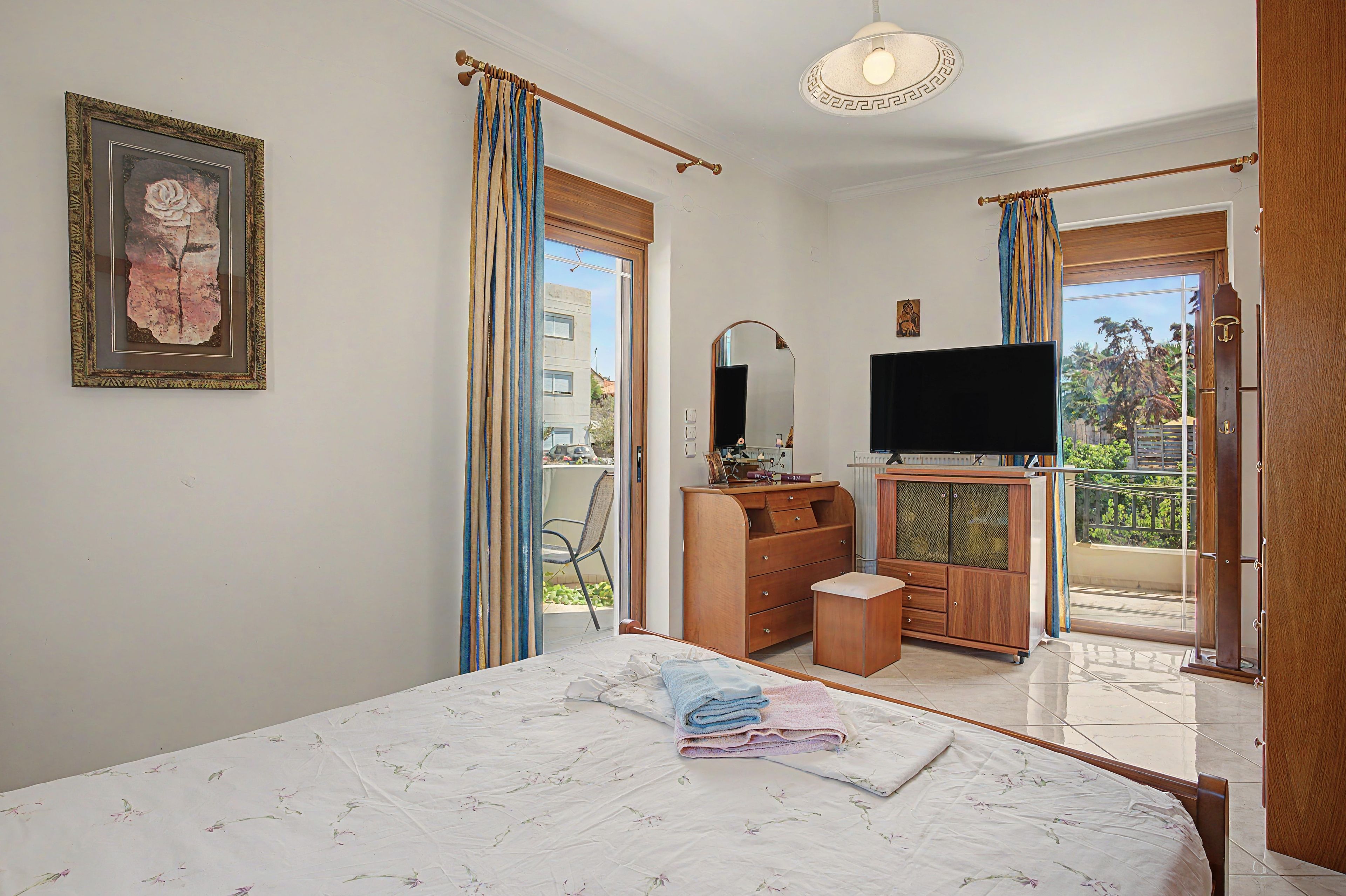 Een slaapkamer met een bed, een televisie, een kaptafel en een balkon met een stoel.