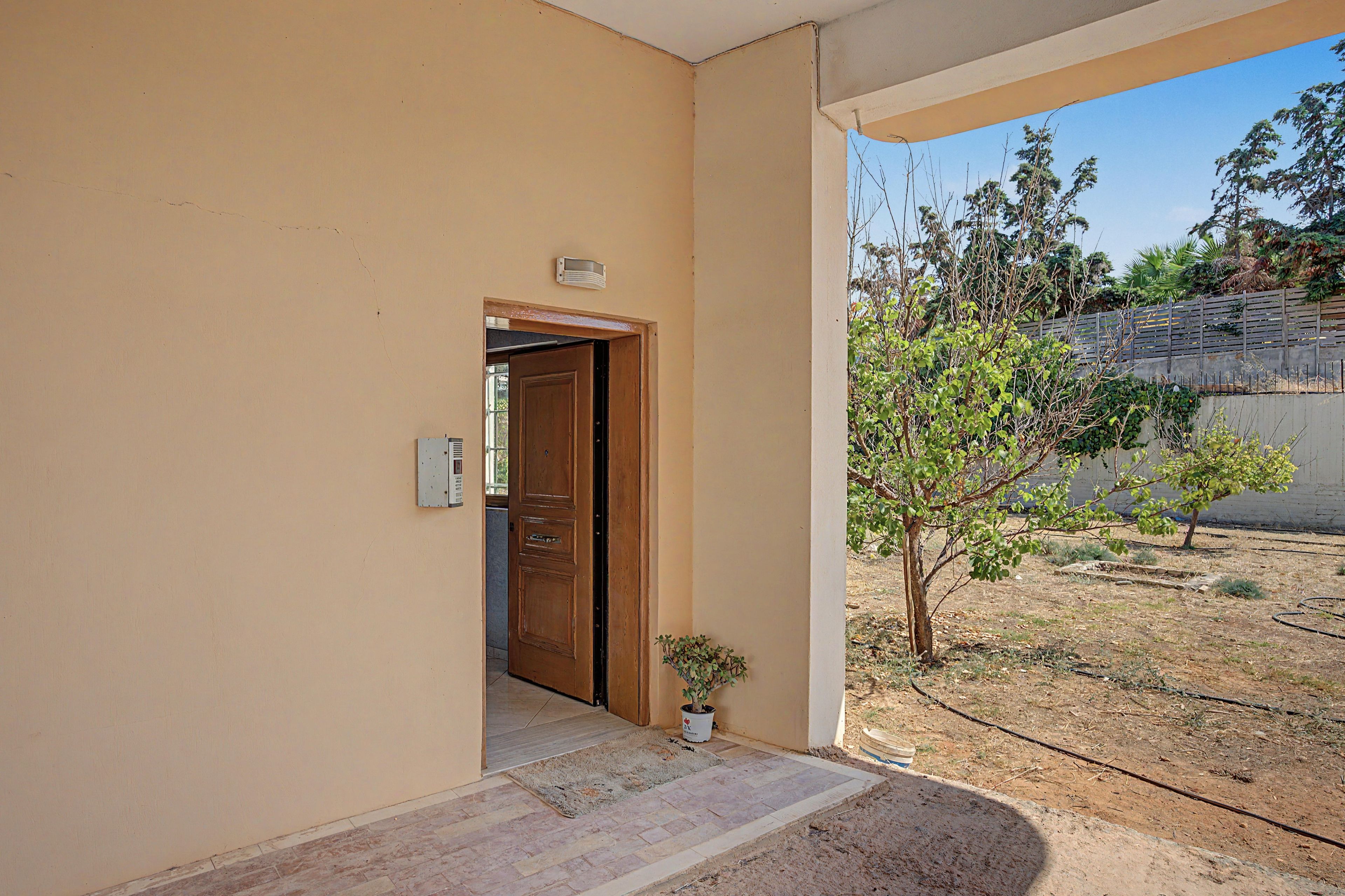 A beige exterior wall with a wooden door leading to an indoor space.