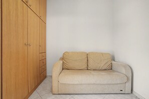 Een kamer met een houten garderobe en een beigekleurde bank tegen een effen muur.