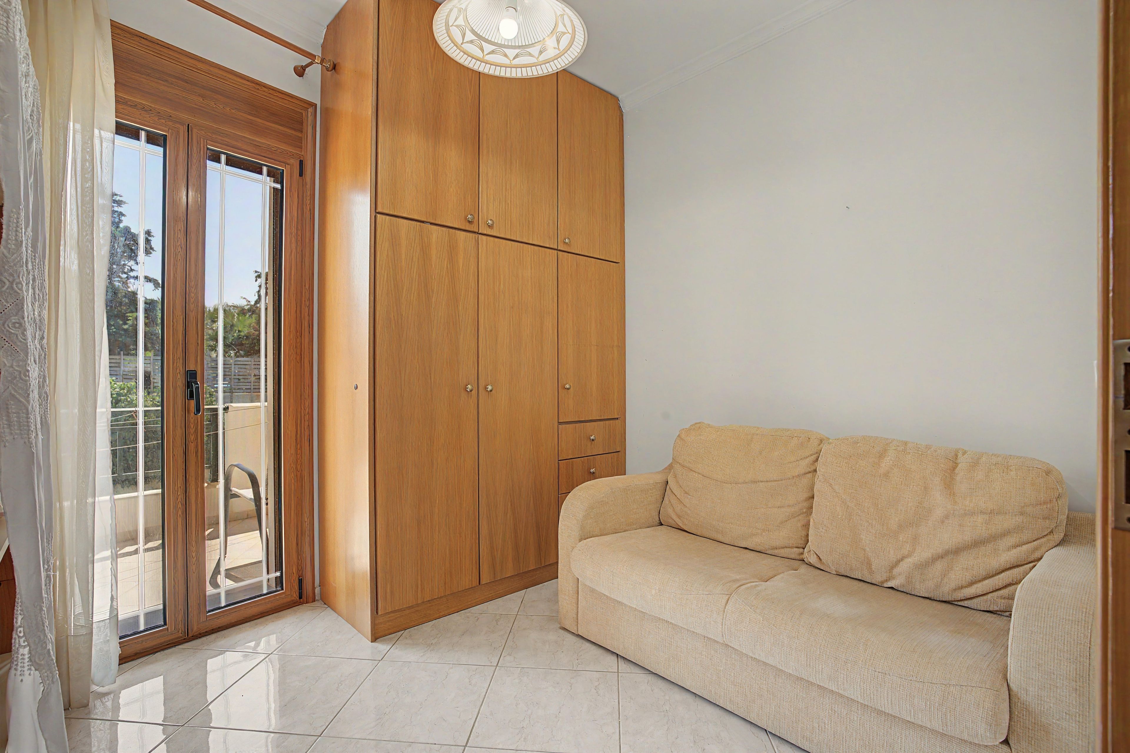 A room with a sliding glass door, a wooden wardrobe, and a beige sofa.