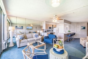 A spacious living area with a sofa, a blue armchair, a coffee table with fruit, and a kitchen area with a microwave and refrigerator. - Beautiful Ocean View Condo Maui Sunset Resort Sleeps 4! (Kihei)