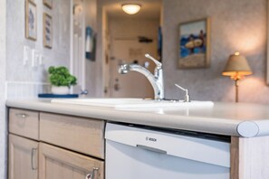 A kitchen with a Bosch dishwasher, a white countertop, a sink with a modern faucet, and a potted plant on the counter. - Beautiful Ocean View Condo Maui Sunset Resort Sleeps 4! (Kihei)