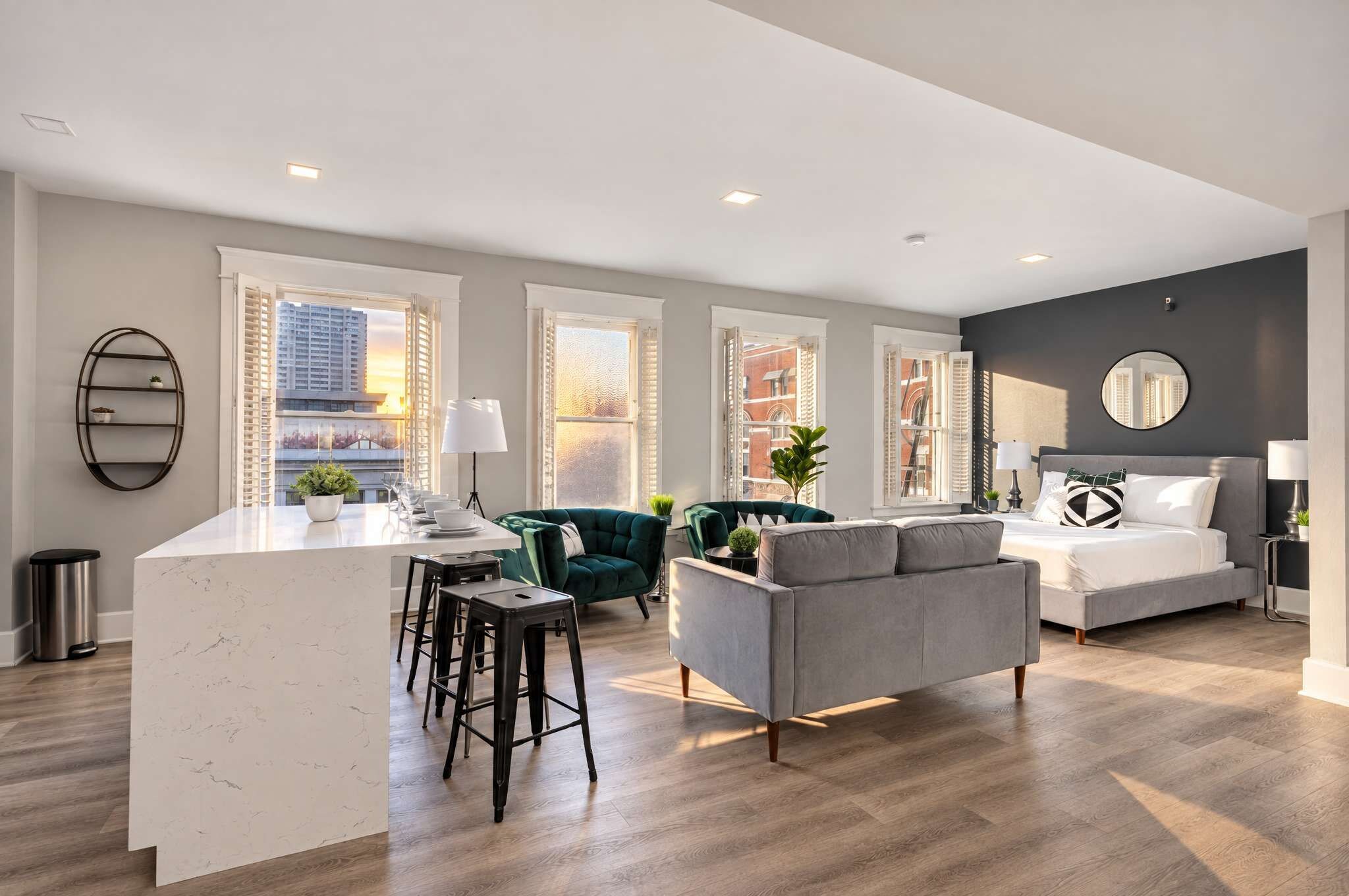 A modern apartment with a kitchen island, seating area, and a bedroom with a large bed and a round mirror.
