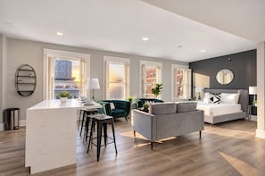 A modern apartment with a kitchen island, seating area, and a bedroom with a large bed and a round mirror. - The Penn Hotel - Premium Beds & Gaslamp Nightlife! (San Diego)