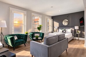 A modern living room with a grey sofa, green armchairs, a round coffee table, and a bed with a grey headboard. - The Penn Hotel - Premium Beds & Gaslamp Nightlife! (San Diego)