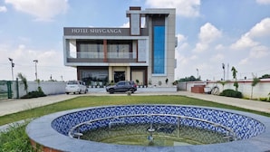 Un hotel llamado 'HOTEL SHIVGANGA' con un diseño moderno, una piscina y un estacionamiento.