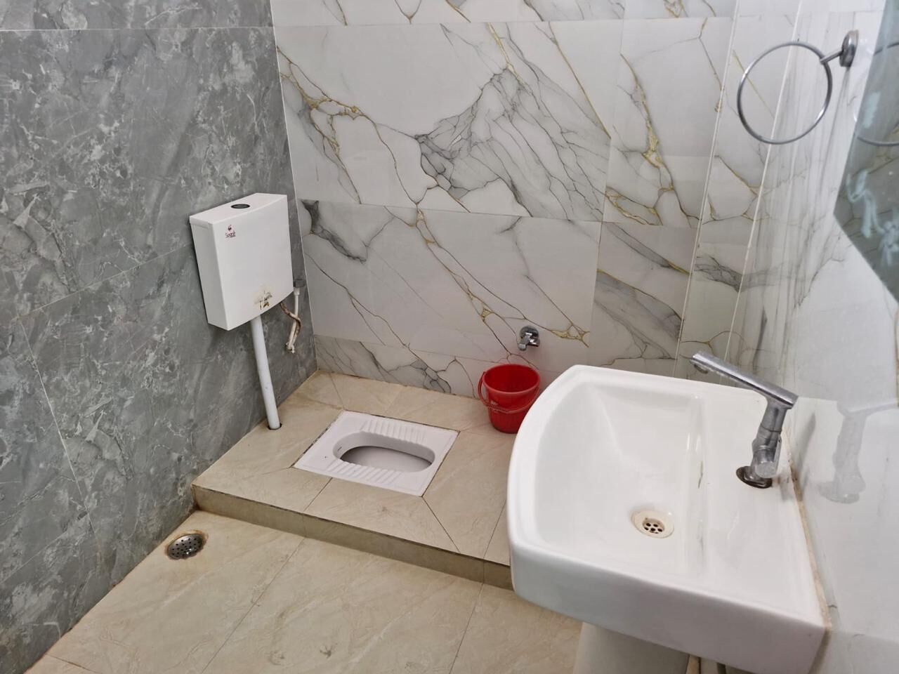 Un baño con inodoro, lavamanos, un cubo rojo y una pared con diseño de mármol.