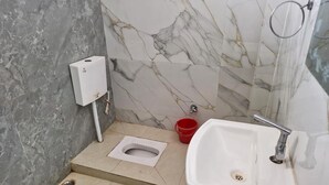 Un baño con inodoro, lavamanos, un cubo rojo y una pared con diseño de mármol.