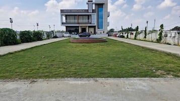 Un moderno edificio de hotel con un letrero que dice 'HOTEL SHIVGANGA' y un césped ajardinado con una fuente circular.