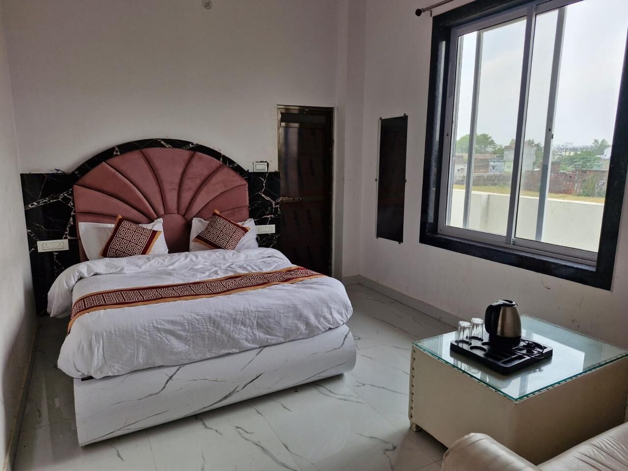 Una camera d'albergo con un letto, un comodino con un bollitore, una finestra e una porta.