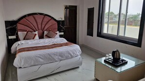 Een hotelkamer met een bed, een nachtkastje met een waterkoker, een raam en een deur.