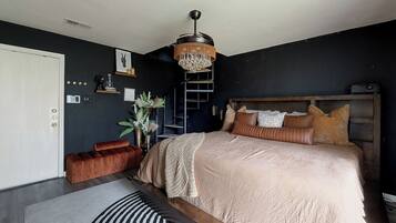A bedroom with a bed, a ladder, a hanging light fixture, and a door.