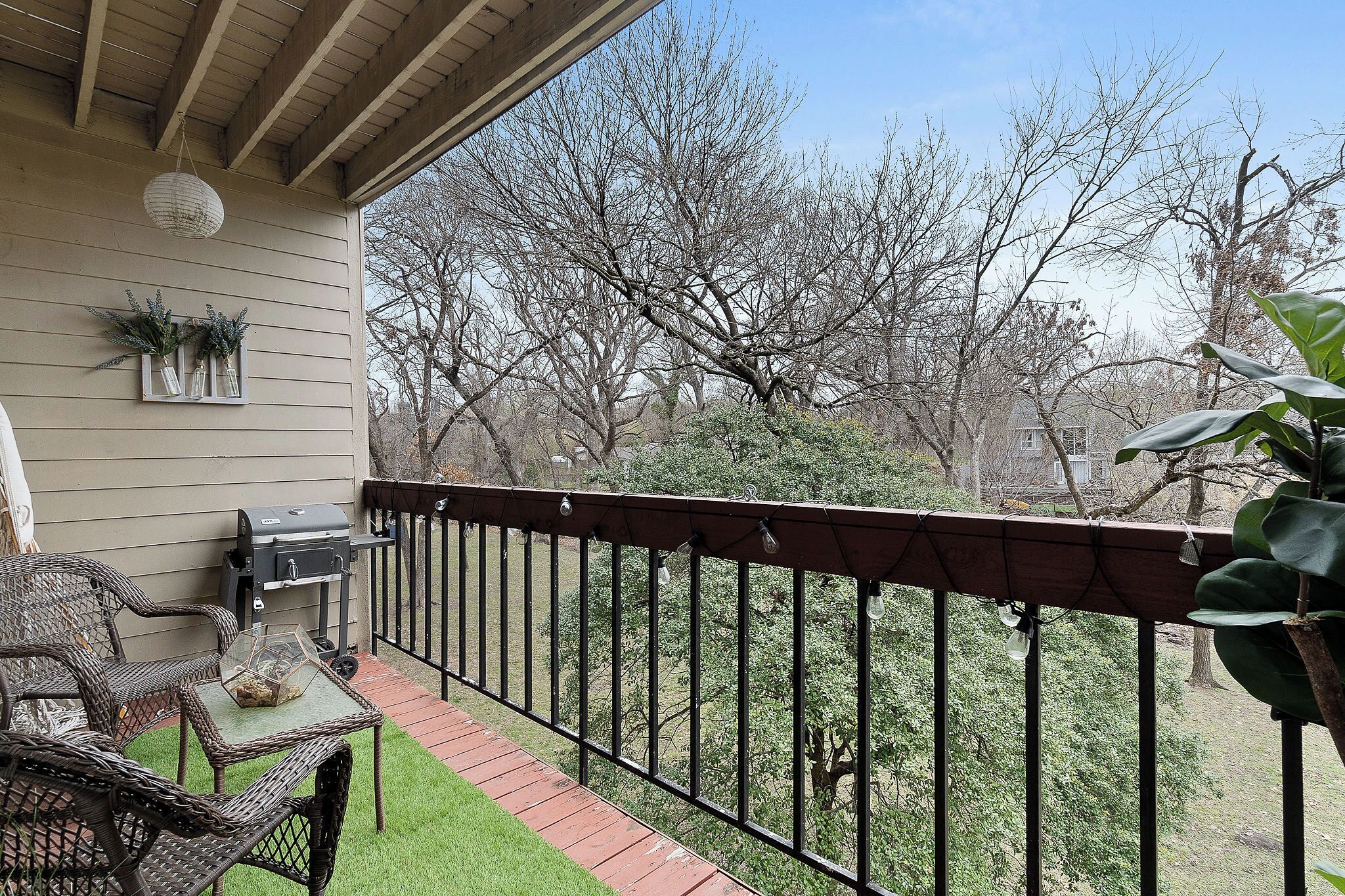 A wooden deck with outdoor furniture, a grill, and a view of trees.