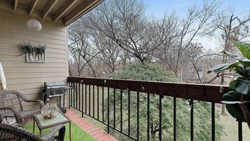 A wooden deck with outdoor furniture, a grill, and a view of trees.