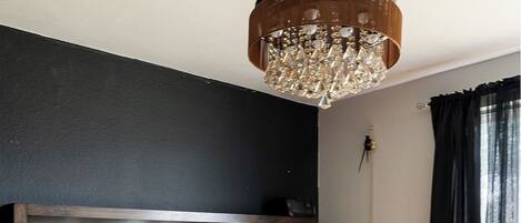 A bedroom with a large bed, a wooden headboard, a chandelier, and a window with curtains.