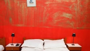 A bed with white bedding, two bedside tables with lamps, and a red wall with a framed picture. - Résidence Ahlem Tozeur (Tozeur)