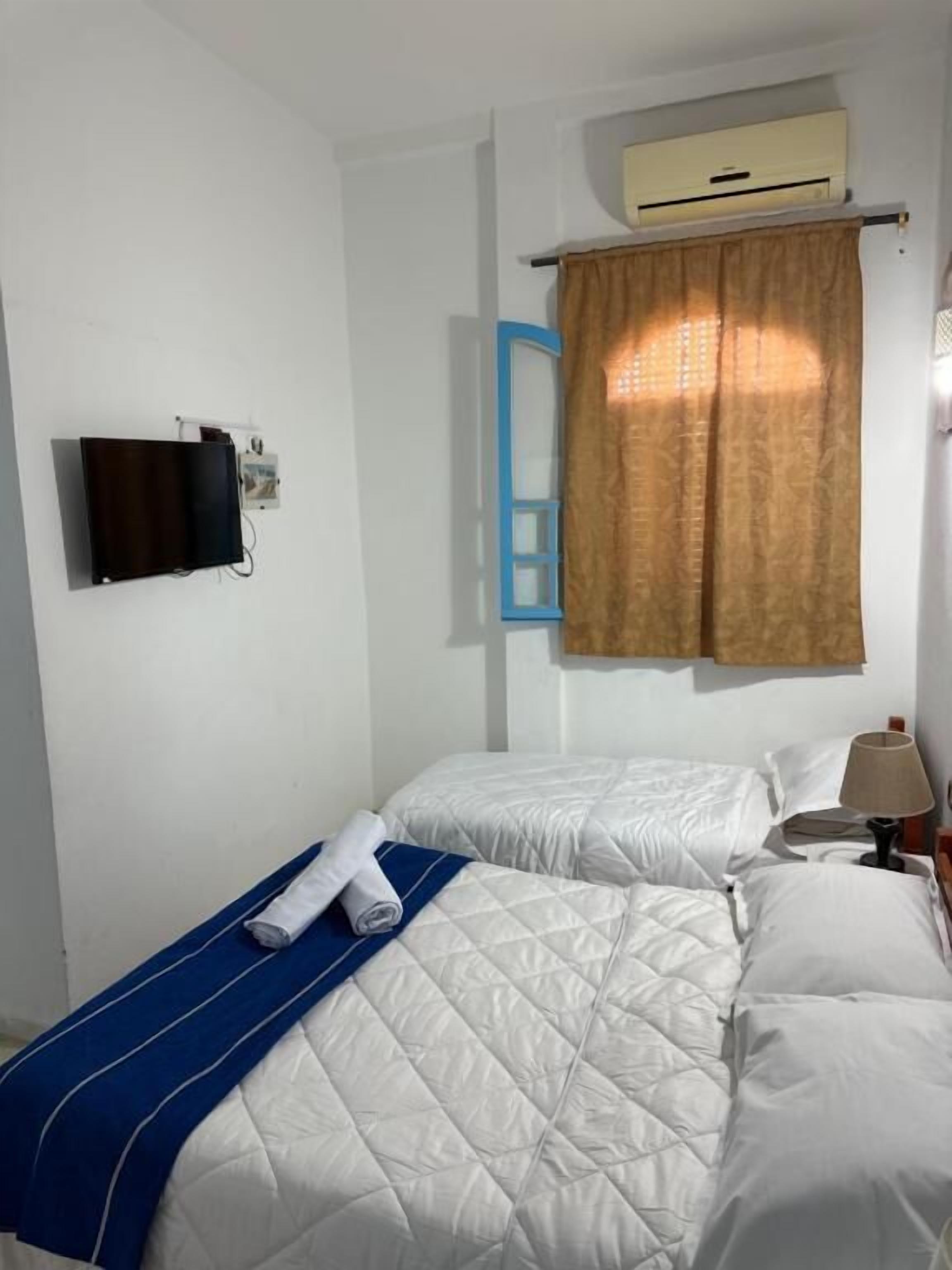 A hotel room with two beds, a TV, an air conditioner, and a window with curtains.