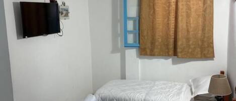 A hotel room with two beds, a TV, an air conditioner, and a window with curtains.