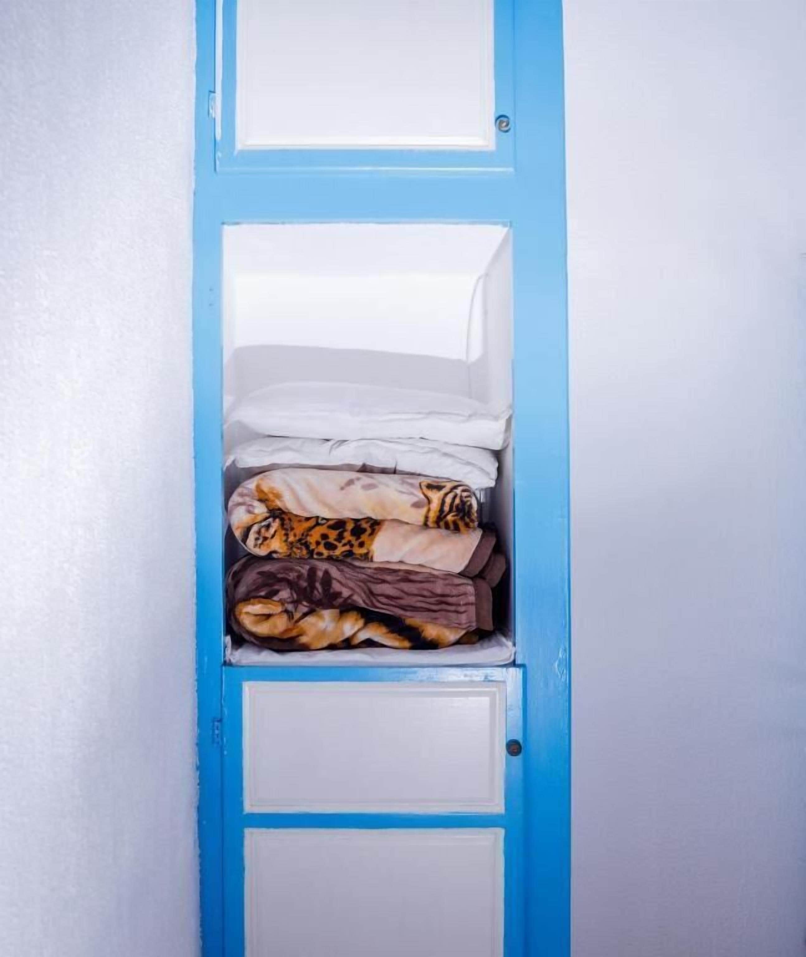 A blue wardrobe with multiple compartments, some containing folded clothes.