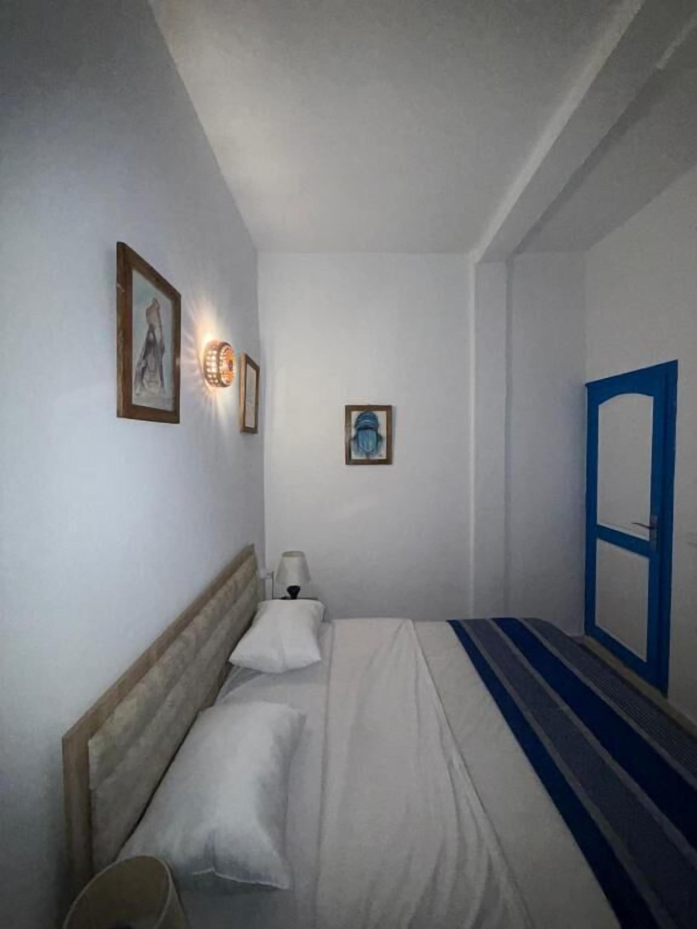 A single bed with a headboard, a bedside table with a lamp, and a wall-mounted light fixture.