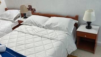 Habitación de hotel con dos camas, una mesita de noche de madera con lámparas, una alfombra estampada y un cuadro en la pared.