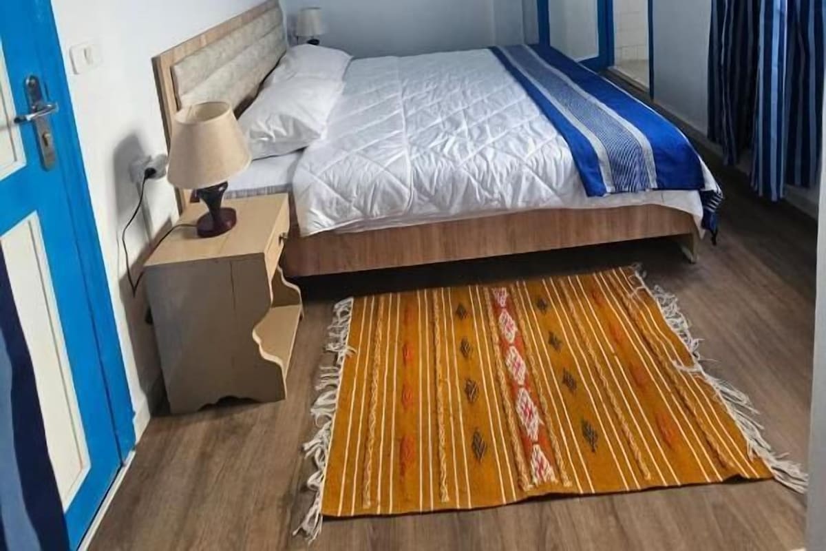 Een slaapkamer met een bed, nachtkastje en een raam met gordijnen.