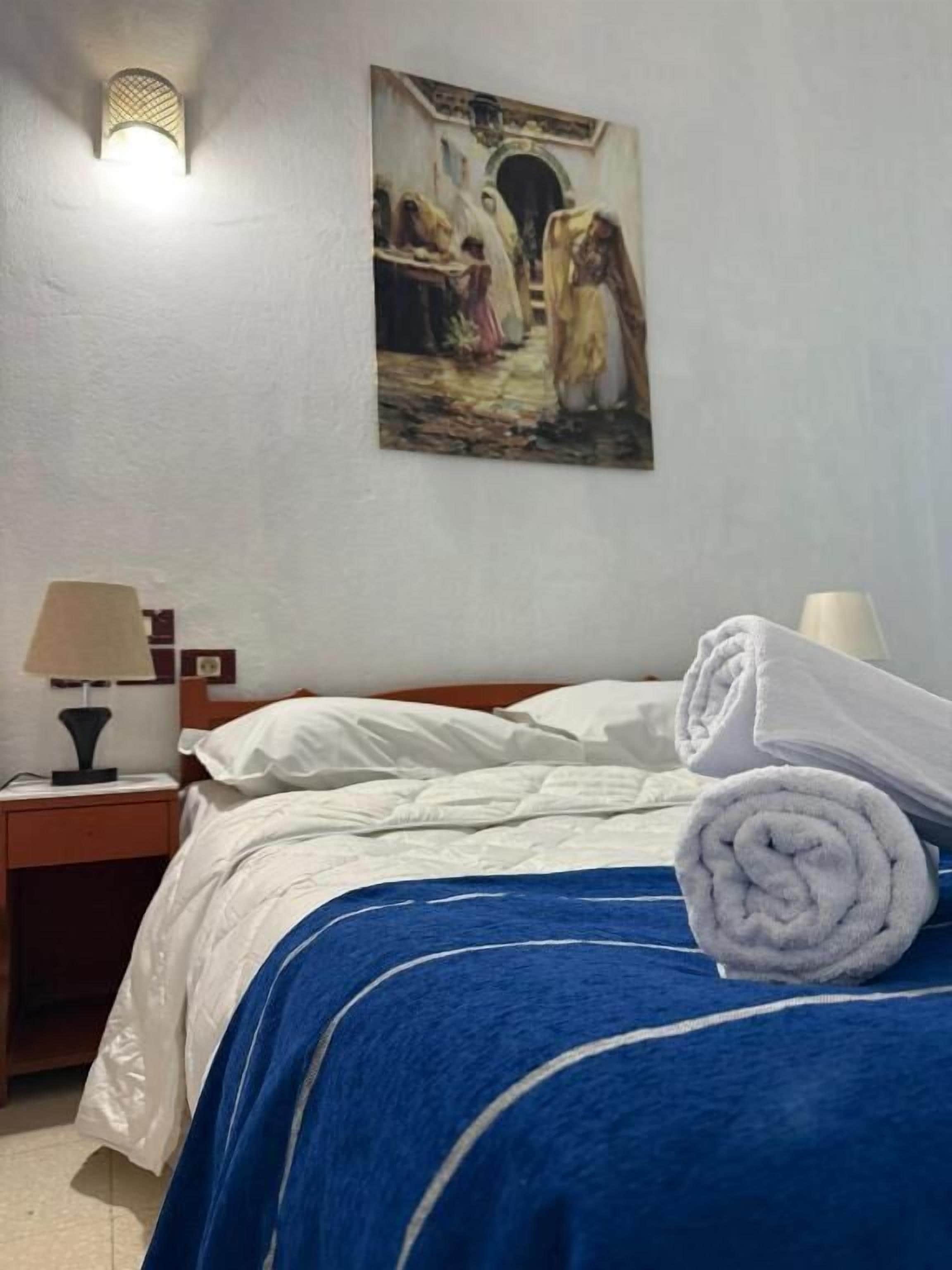 Una habitación de hotel con una cama, una mesita de noche, una lámpara y un cuadro en la pared.
