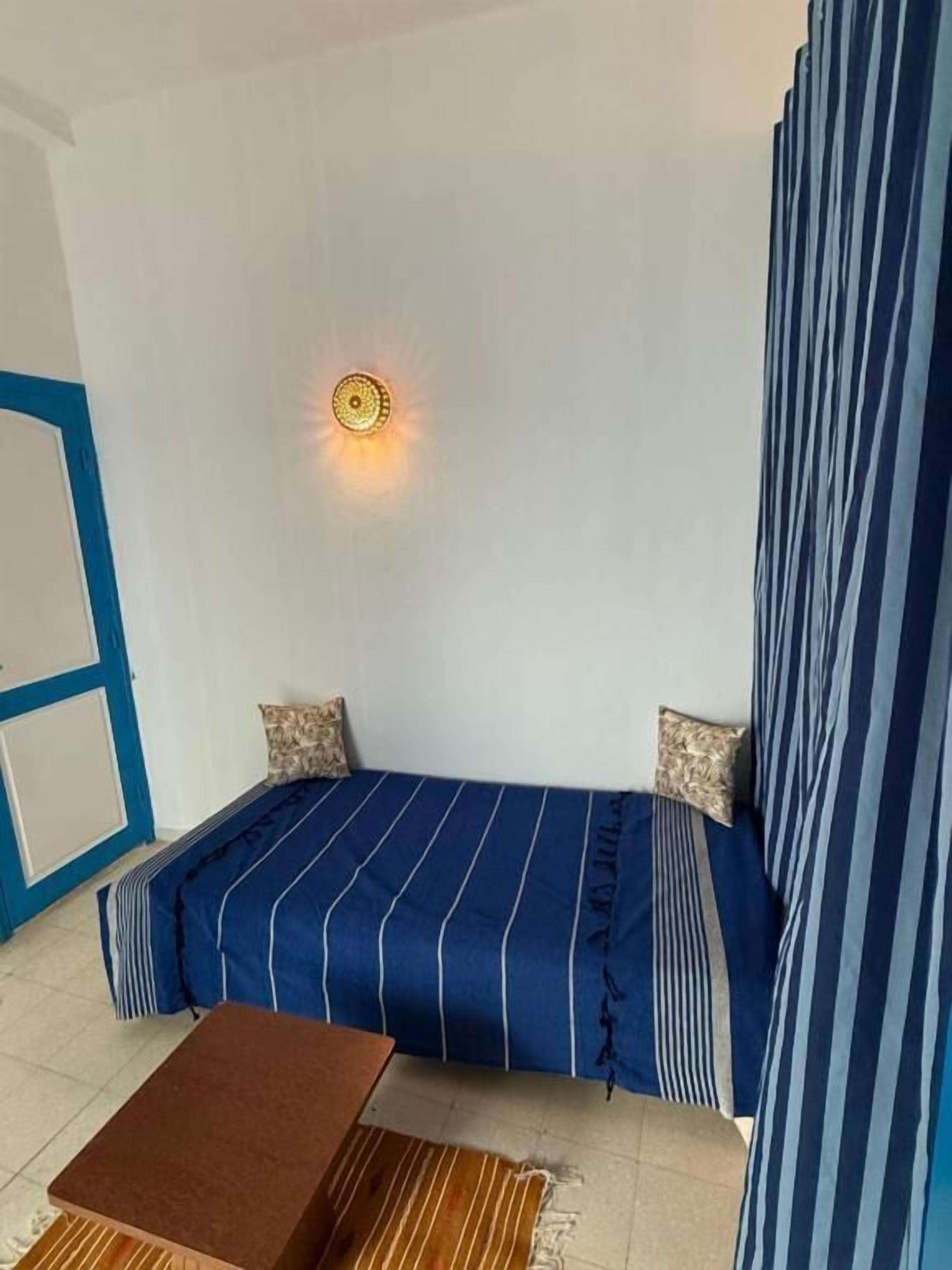 Une chambre avec un lit simple, une petite table et un luminaire fixé au mur.