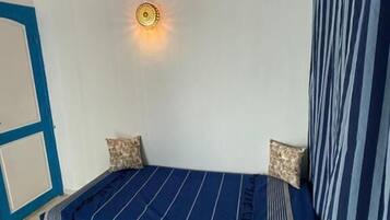 Une chambre avec un lit simple, une petite table et un luminaire fixé au mur.