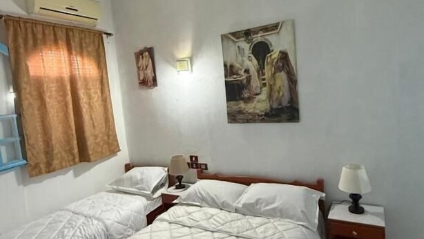 A bedroom with two beds, a nightstand, a lamp, and a painting on the wall. - Résidence Ahlem Tozeur (Tozeur)