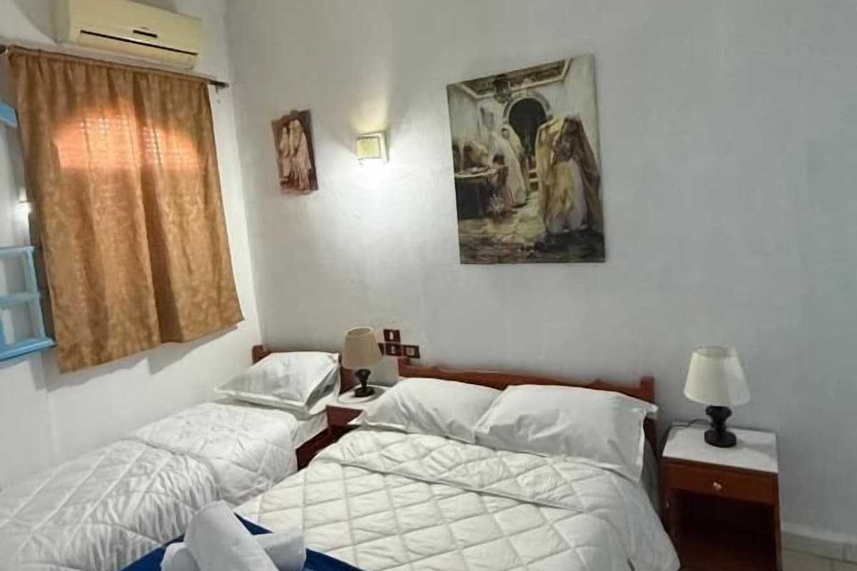 Een slaapkamer met twee bedden, een nachtkastje, een lamp en een schilderij aan de muur.