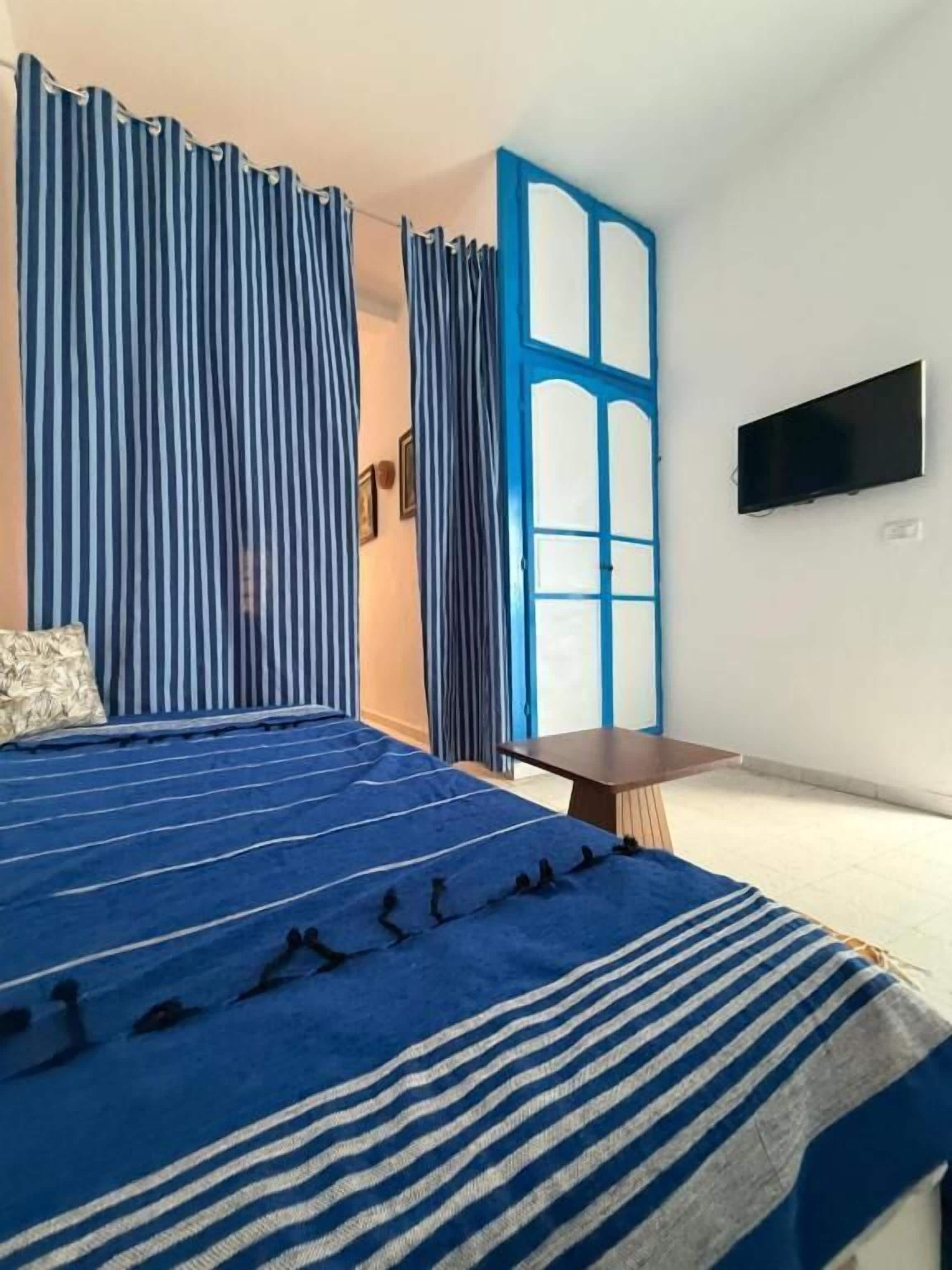 Un dormitorio con cama, cortinas, televisor y una mesita.