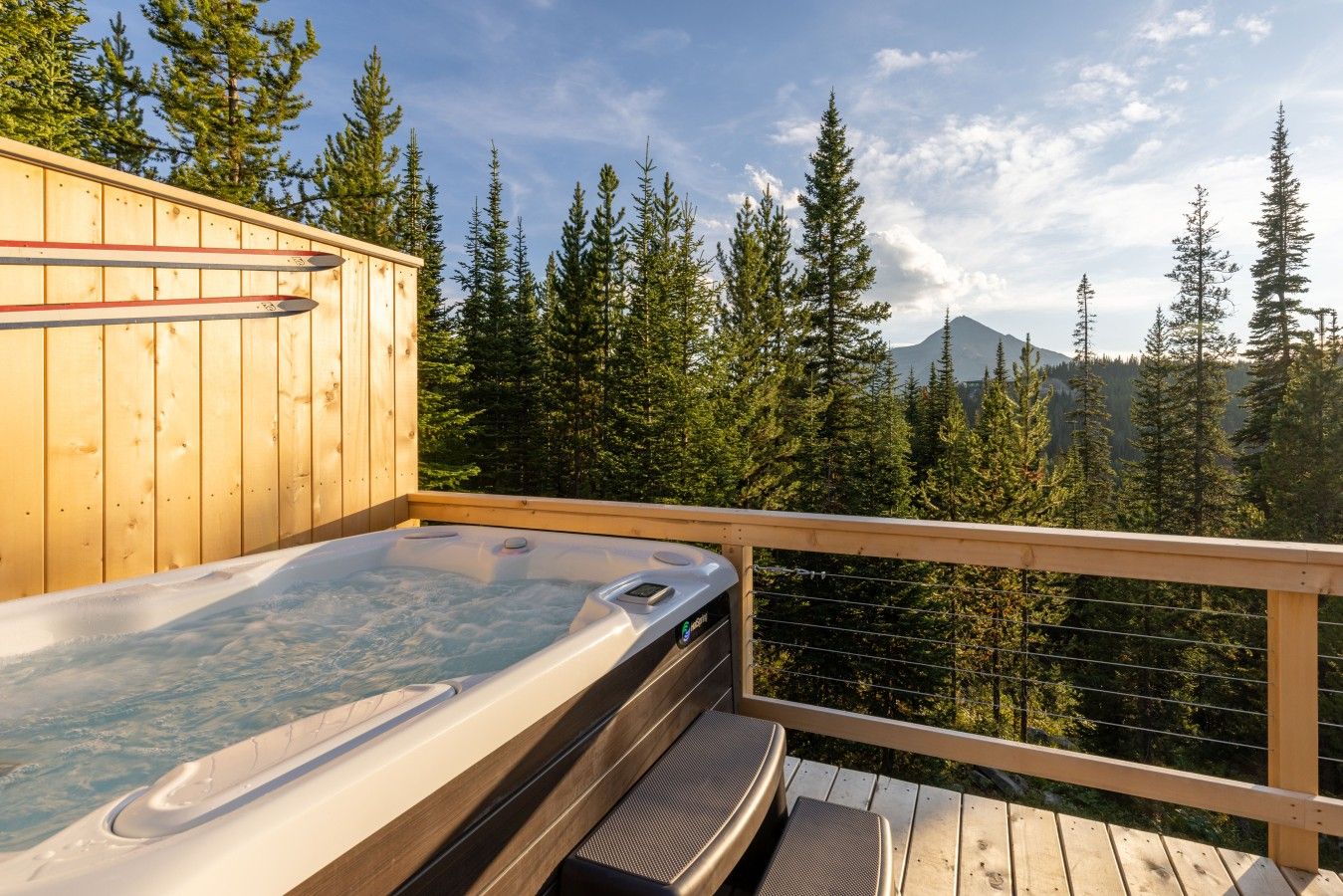 A hot tub on a wooden deck with a view of a forest and mountains.