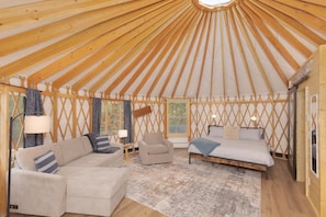 A yurt interior with a sofa, armchair, and bed, wooden beams, and a window. - Beehive Basin Yurt: Stunning Mountain Views, Private Hot Tub (Big Sky)