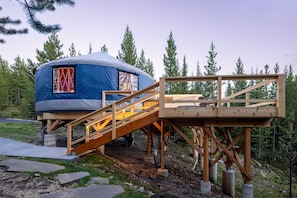 A blue tent with a wooden deck and stairs, set in a forested area.