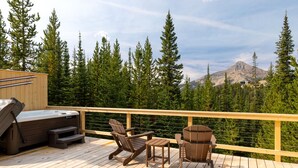 Um deck de madeira com hidromassagem, duas cadeiras Adirondack e vista para uma cordilheira.
