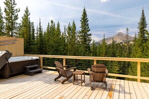 A wooden deck with a hot tub, two Adirondack chairs, and a view of a mountain range. - Beehive Basin Yurt: Stunning Mountain Views, Private Hot Tub (Big Sky)