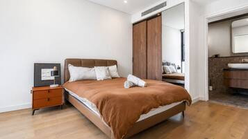 A modern bedroom with a large bed, a nightstand, a mirror, and a bathroom visible through an open door.