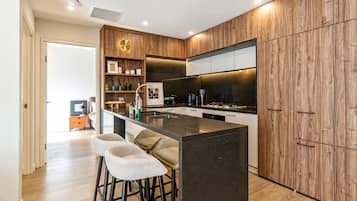 A modern kitchen with a central island, bar stools, wooden cabinetry, and a built-in oven.