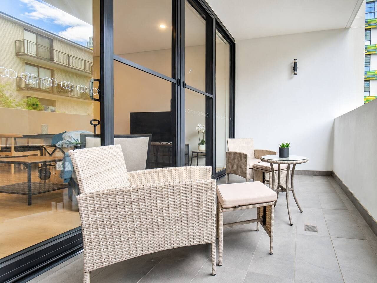 A balcony with wicker furniture, a glass door, and a view of a building with balconies.