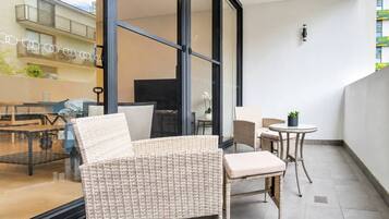 A balcony with wicker furniture, a glass door, and a view of a building with balconies.