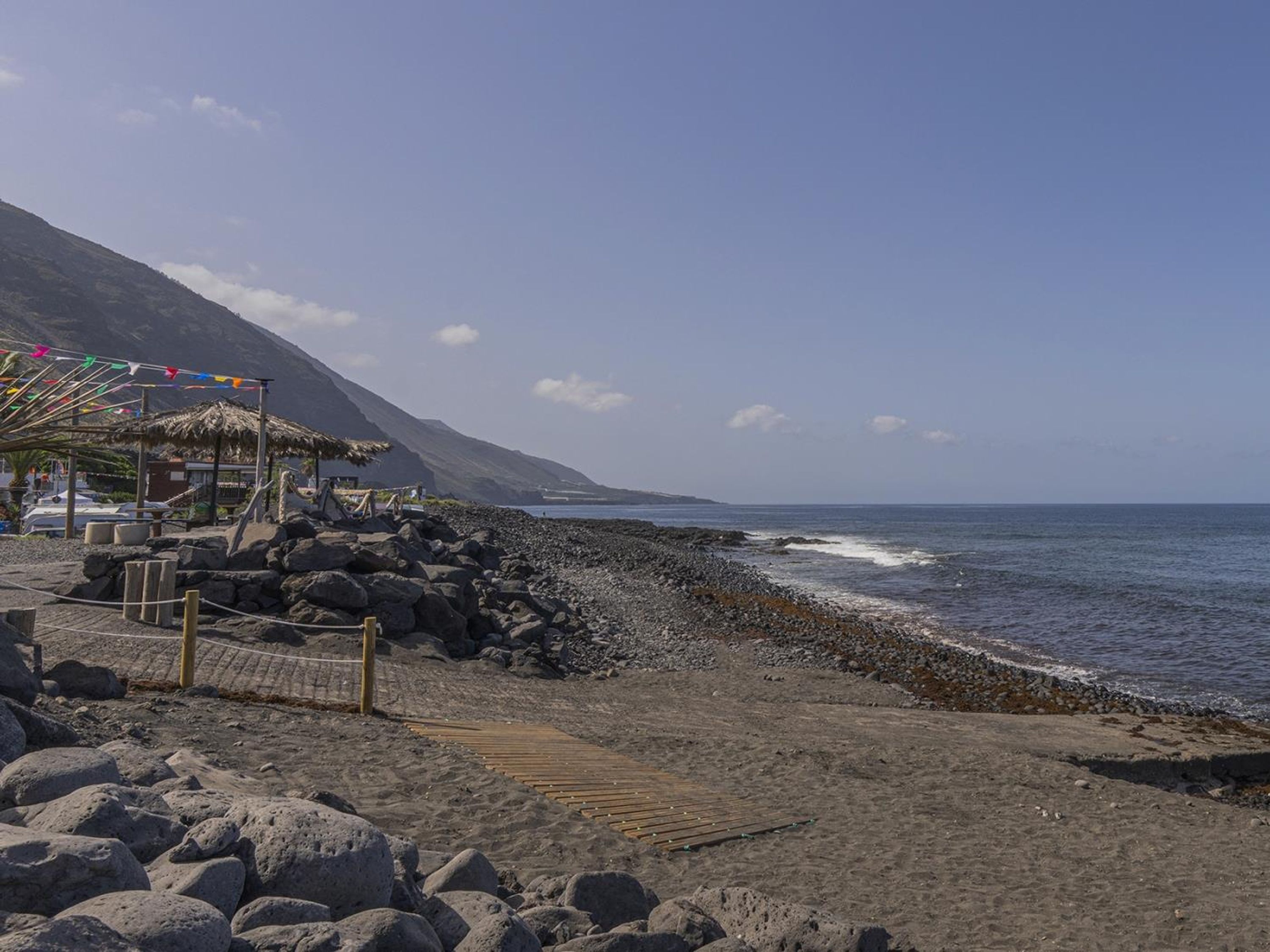 Une plage avec une structure à toit de chaume, une promenade en bois et une côte rocheuse.