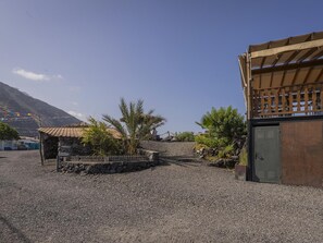 Un espace de stationnement recouvert de gravier, avec un petit bâtiment en pierre, une structure en bois dotée d’un toit et une porte en métal.