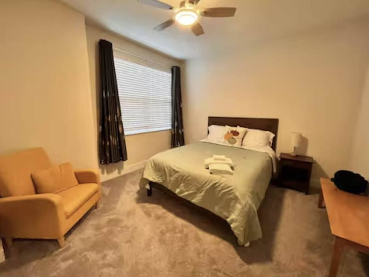 A bedroom with a bed, a nightstand, a chair, and a ceiling fan.