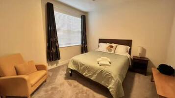 A bedroom with a bed, a nightstand, a chair, and a ceiling fan.