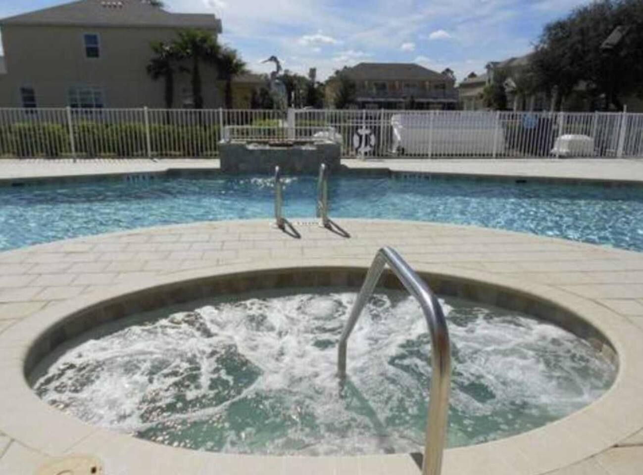 A hot tub with a metal railing, surrounded by a pool and a fence.