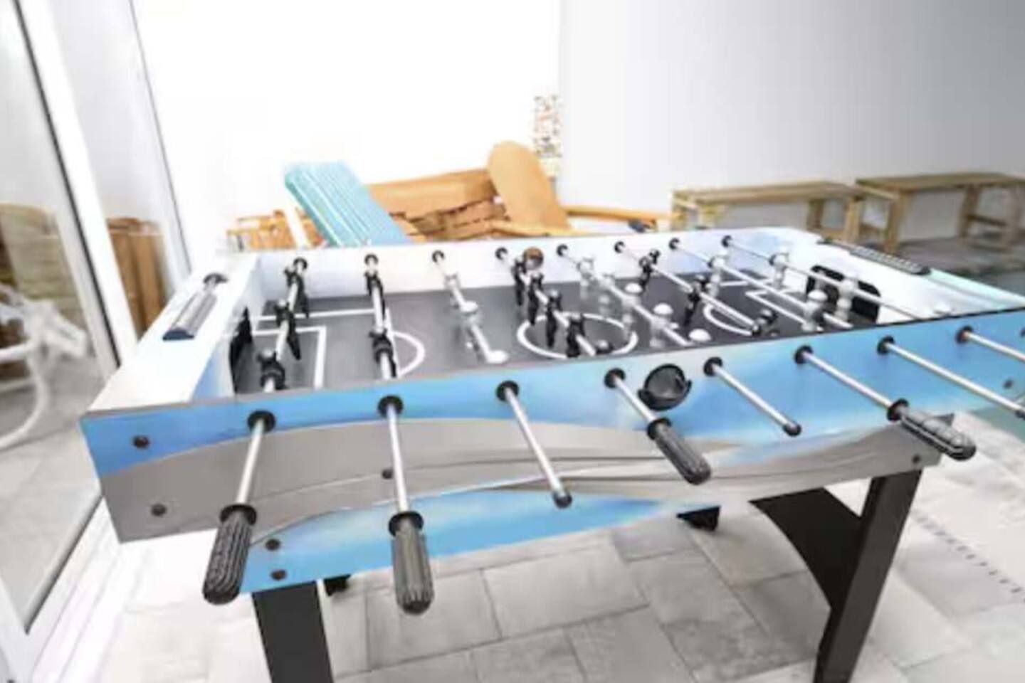 A foosball table in a room with a large window, a chair, and a table.