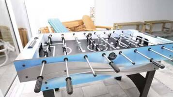 A foosball table in a room with a large window, a chair, and a table.