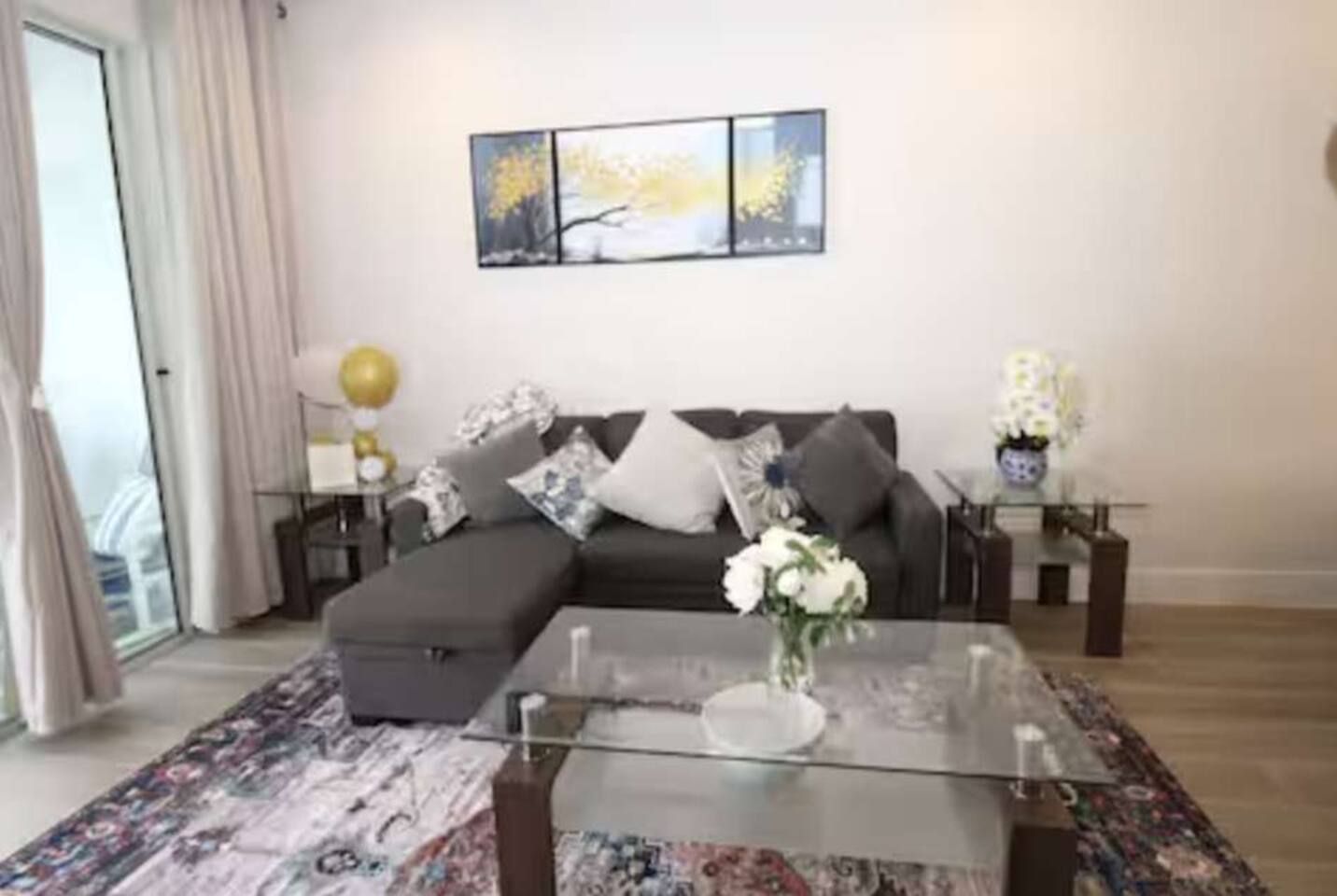 A modern living room with a sectional sofa, a glass coffee table, and a patterned rug.