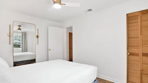 A bedroom with a bed, a ceiling fan, a mirror, and a wooden door.